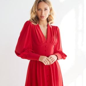 May include: A red long-sleeved dress with a V-neckline and a button-up front. The dress has a fitted bodice and a flowing skirt.