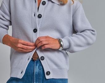 May include: A light blue cardigan with a collared neckline and black buttons. The ribbed knit sweater is paired with blue jeans and a silver bracelet. The cardigan is buttoned up.
