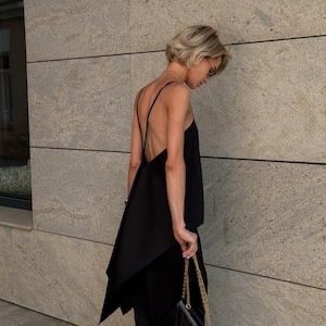 以下が含まれることがあります： 非対称のデザインのノースリーブトップスと、お揃いのパンツを組み合わせた黒の服装。ゴールドチェーンストラップの小さなキルティングブラックハンドバッグが手に持たれています。短いブロンドの髪の人がこの服装を着ています。