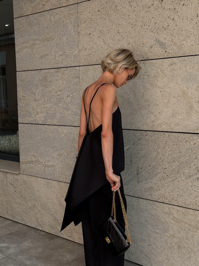 以下が含まれることがあります： 非対称のデザインのノースリーブトップスと、お揃いのパンツを組み合わせた黒の服装。ゴールドチェーンストラップの小さなキルティングブラックハンドバッグが手に持たれています。短いブロンドの髪の人がこの服装を着ています。