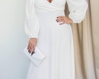 May include: A white midi dress with long, puffy sleeves and a sweetheart neckline. The dress is paired with white heels and a white clutch. The clutch has a black logo. The dress is a solid color and appears to be made of a soft fabric.