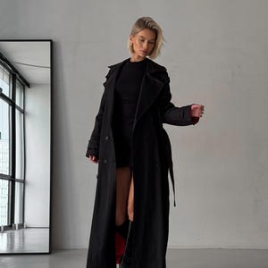 May include: A long black trench coat with a red lining. The coat has a double-breasted closure, a belt, and a collar.