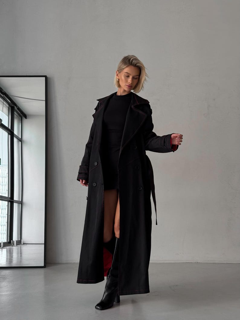 May include: A long black trench coat with a red lining. The coat has a double-breasted closure, a belt, and a collar.