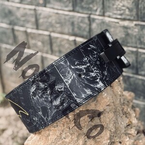 Peut inclure: Ceinture d'halt&eacute;rophilie noire avec un design de bande dessin&eacute;e repr&eacute;sentant Batman et Robin. La ceinture a une boucle noire et est faite d'un mat&eacute;riau durable. La ceinture repose sur un rocher.