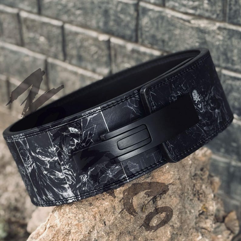 Peut inclure: Une ceinture d'halt&eacute;rophilie noire avec un motif marbr&eacute; et une boucle noire. La ceinture est fabriqu&eacute;e dans un mat&eacute;riau durable et est con&ccedil;ue pour soutenir les exercices d'halt&eacute;rophilie. La ceinture est pr&eacute;sent&eacute;e sur une roche.