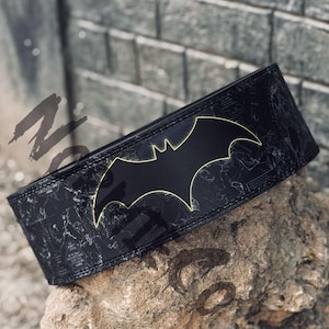Peut inclure: Ceinture d'halt&eacute;rophilie noire avec le logo Batman brillant et un contour jaune. Le fond noir est orn&eacute; d'illustrations de style bande dessin&eacute;e. Con&ccedil;ue pour l'halt&eacute;rophilie et l'entra&icirc;nement en force, elle mesure environ 10 cm de large.