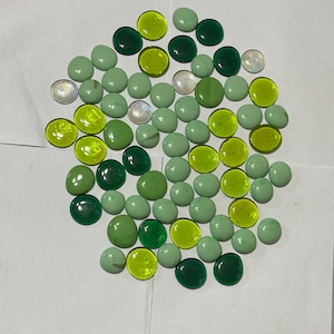 Peut inclure: Une collection de galets en verre vert, jaune et transparent. Les galets sont lisses et ronds, et ils sont disposés en cercle lâche.