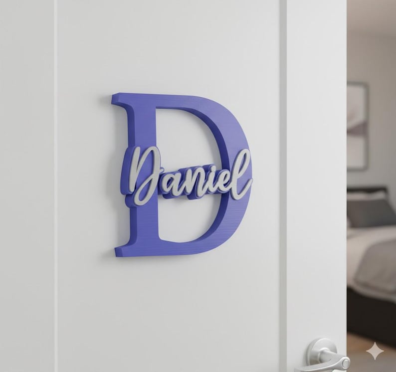 May include: A purple wooden letter "D" with the name "Daniel" in a cursive font. The name is in a lighter color, creating a layered effect. The sign is mounted on a white door.