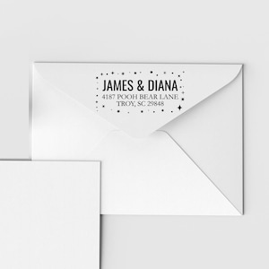 May include: A white envelope with black text that reads "JAMES & DIANA" above the address "4187 POOH BEAR LANE TROY, SC 29848". The text is surrounded by small star illustrations.