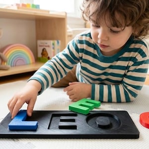 May include: A child's wooden puzzle with the letters L, E, and O in blue, green, and red. The letters fit into a black wooden base. The child is wearing a striped shirt. Educational toy.
