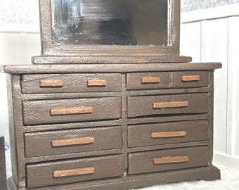 May include: Miniature brown wooden dresser with eight drawers and a rectangular mirror. The dresser has copper-colored drawer pulls and a dark brown finish. The mirror is framed in the same brown wood.