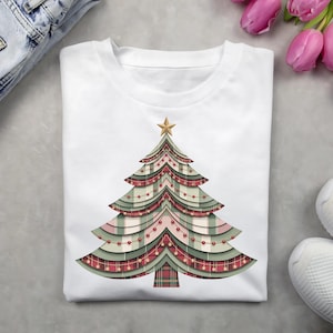 Könnte beinhalten: Weißes T-Shirt mit einem Weihnachtsbaum-Design. Der Baum ist mit rot-grünen Karomustern, roten Lichtern und einem goldenen Stern verziert. Ein festlicher Artikel für die Feiertage.