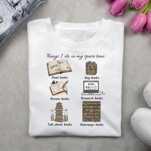 Pode incluir: Camiseta branca com o texto "Things I do in my spare time" e ilustrações de leitura, compra, revisão, pesquisa, conversa e reorganização de livros. A camiseta tem gola redonda e mangas curtas.