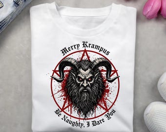 May include: White t-shirt featuring a graphic of Krampus, a horned figure with a long beard and red eyes, surrounded by a red star and the text "Merry Krampus Be Naughty, I Dare You."
