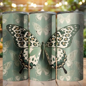 May include: A cylindrical tumbler featuring a repeating pattern of butterflies on a sage green background. The central butterfly design displays intricate black and white wing details with leopard print accents in shades of brown and tan.