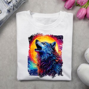 May include: White t-shirt with a colorful wolf howling at the moon graphic. The wolf is blue, purple, and orange, and the moon is yellow and orange. The background is a dark blue with stars.