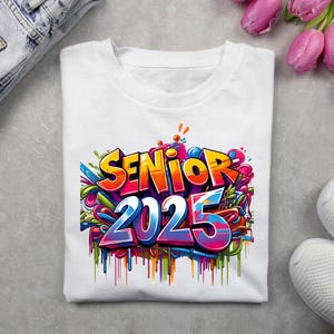 May include: White t-shirt with a colorful graphic design that says "Senior 2025" in a graffiti style.