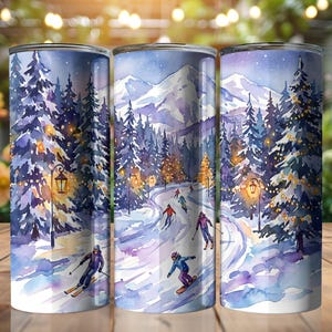 May include: A set of three stainless steel tumblers with a winter watercolor design. The design features skiers and snowboarders on a snowy slope, with pine trees, street lamps, and mountains in the background. The color palette includes blues, purples, and whites.
