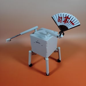 Könnte beinhalten: Ein weißer, kastenförmiger Roboter mit beweglichen Armen und Beinen. Er hält einen weißen und schwarzen Fächer mit roten japanischen Schriftzeichen. Der Roboter hat das Wort "Jetson" auf der Seite. Der Hintergrund ist orange.
