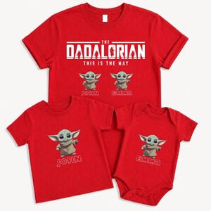 May include: Red t-shirts and a babygrow featuring a cartoon character. The shirts display the text "THE DADALORIAN THIS IS THE WAY" and the character's image. One shirt says "JOHN" and the babygrow says "EMMA".