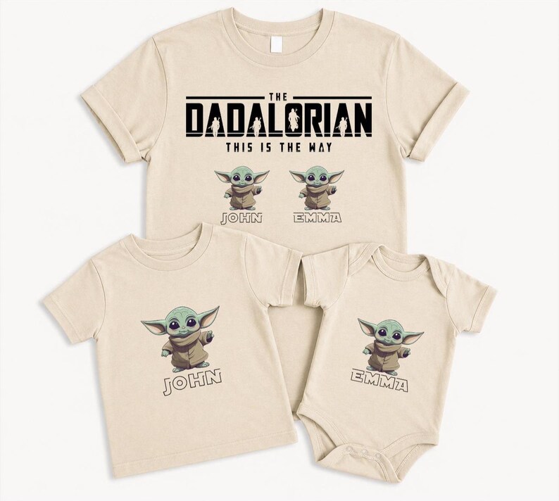May include: Beige t-shirts and a babygrow featuring a green alien character. The adult shirt reads "The Dadalorian, This is the Way." The children's shirts have the names "John" and "Emma" below the character.