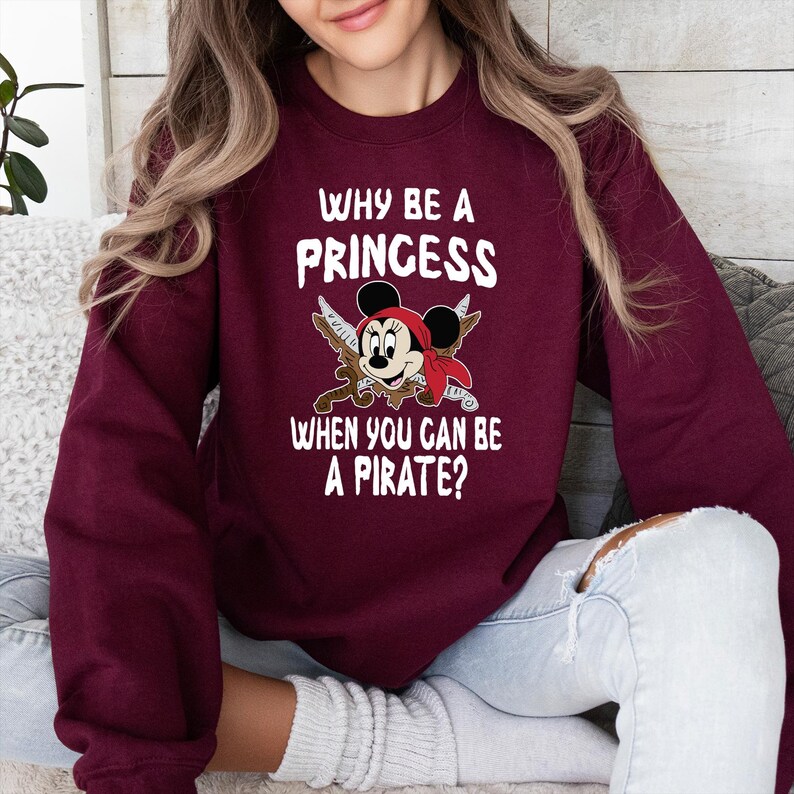 K&ouml;nnte beinhalten: Burgunderfarbenes Sweatshirt mit dem Text "WHY BE A PRINCESS WHEN YOU CAN BE A PIRATE?" und einer Grafik einer Piratenmaus. Die Maus tr&auml;gt ein rotes Bandana und h&auml;lt gekreuzte Schwerter.
