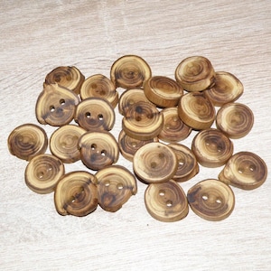 Peut inclure: Un assortiment de boutons en bois d'aspect naturel et rustique. Les boutons sont circulaires, avec un grain de bois visible et deux ou quatre trous pour la couture. Les boutons varient en taille et sont de couleur brun clair.