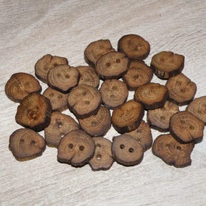 Puede incluir: Una colección de botones de madera marrón, algunos con un acabado de madera natural y otros con una mancha más oscura. Los botones son de varios tamaños y formas, algunos son redondos y otros más irregulares.
