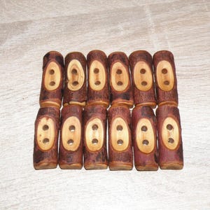 May include: A collection of twelve wooden buttons. Each button is a cylindrical shape with a light-colored oval center and two holes for sewing. The buttons are a mix of brown and tan colors.