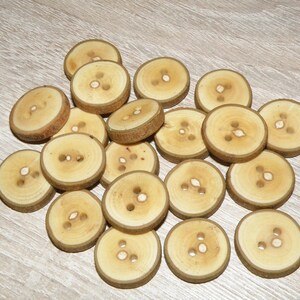 Könnte beinhalten: Ein Haufen natürlicher Holzknöpfe in hellbrauner Farbe mit mehreren Löchern in der Mitte. Die Knöpfe sind in einem zufälligen Muster auf einer hellbraunen Holzoberfläche angeordnet.