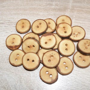 Peut inclure: Une collection de boutons en bois ronds et brun clair, chacun doté de deux trous centraux et d'un bord en écorce brun foncé visible. Les boutons varient légèrement en taille et en grain, affichant des textures de bois naturelles.