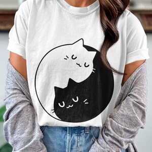 May include: White t-shirt with a black and white yin yang design featuring two cats. The cats are facing each other with their eyes closed and have a cute expression.