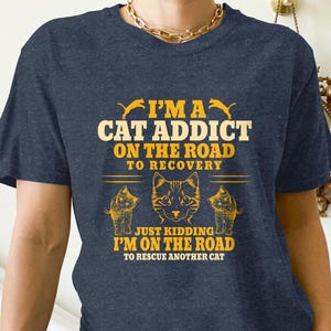 a man wearing a blue t - shirt that says i'm a cat addict