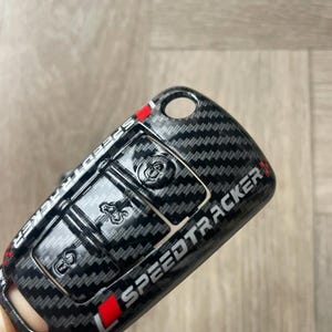 May include: Black carbon fibre key fob cover with a red and white Speedtracker logo.