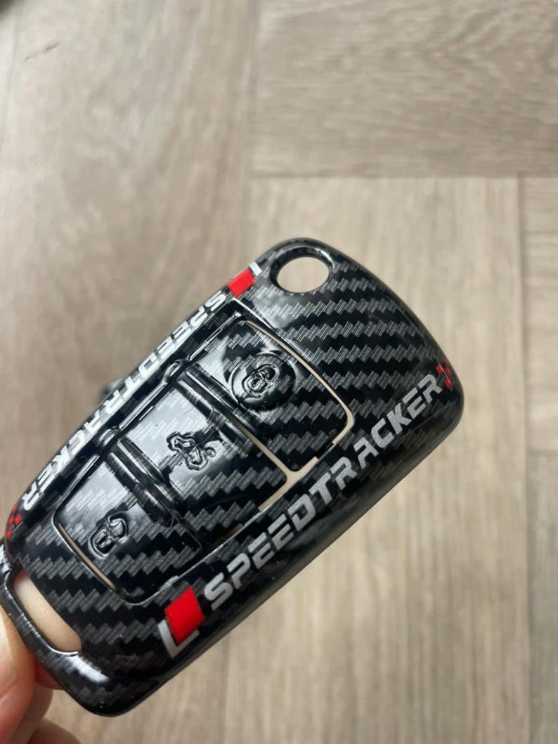 May include: Black carbon fibre key fob cover with a red and white Speedtracker logo.