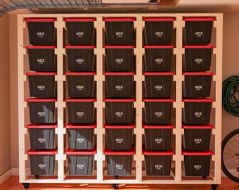 May include: A wooden storage shelf with 25 black storage bins with red lids. The bins are labeled "HDX 37 gal". The shelf has wheels and is in a garage setting.