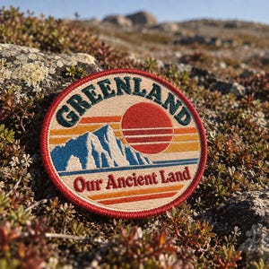 May include: A circular embroidered patch featuring a landscape design with a blue mountain range, a red sun, and horizontal stripes in yellow and orange. The text GREENLAND is arched at the top, and Our Ancient Land is printed at the bottom.