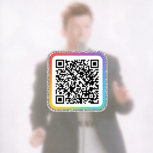 May include: A square sticker featuring a black and white QR code centered on a white background. The sticker has a vibrant rainbow-colored border and a shimmering, glittery silver outer edge, creating a distinct contrast against the background.