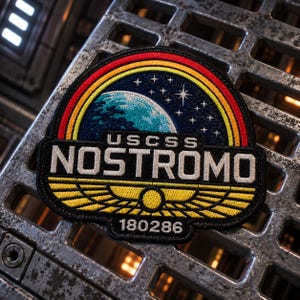 May include: A circular embroidered patch featuring a blue planet and white stars against a dark background, framed by a red, orange, and yellow rainbow arch. The text USCSS NOSTROMO is centred above a yellow winged emblem and the number 180286.