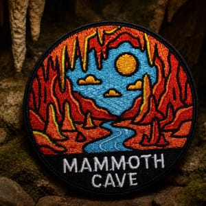 Può includere: Toppa ricamata circolare raffigurante una scena di grotta con cielo blu, sole e fiume. La toppa ha un bordo nero e le parole "MAMMOTH CAVE" in bianco. Il design utilizza colori rosso, arancione, giallo e blu.