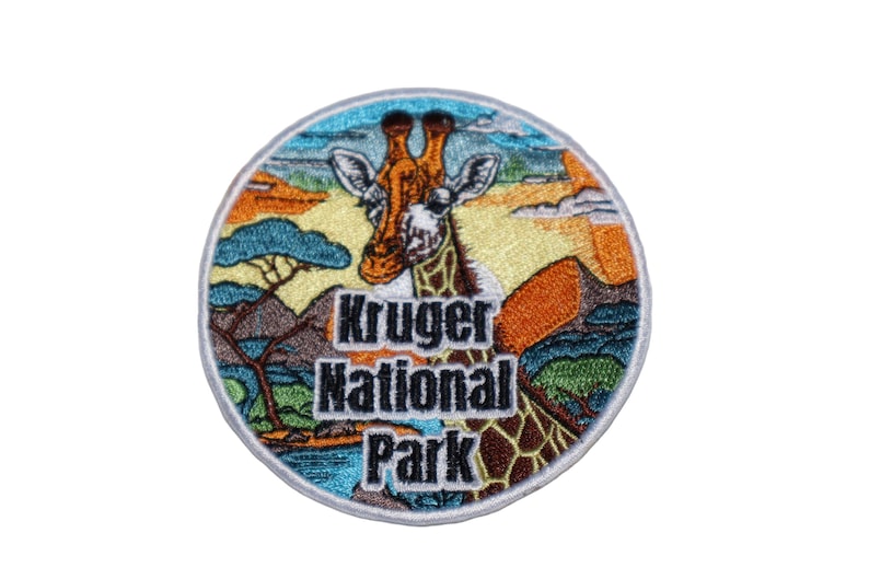 May include: A round embroidered patch with a colorful image of a giraffe in a savanna landscape. The text "Kruger National Park" is printed in black letters below the giraffe.