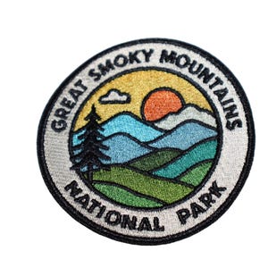 May include: Embroidered patch featuring a scenic design of the Great Smoky Mountains National Park. The patch has a circular shape with a black border and includes text, a sunset, mountains, and a pine tree.
