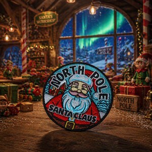 Puede incluir: Parche bordado redondo con Santa Claus, con las palabras "North Pole" y "Santa Claus". El parche tiene un esquema de color azul y rojo. El fondo muestra una escena navideña festiva.
