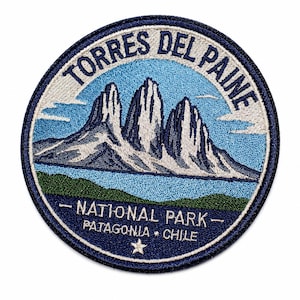May include: A circular embroidered patch featuring a landscape of the Torres del Paine mountains in white and blue. The text reads TORRES DEL PAINE, NATIONAL PARK, and PATAGONIA CHILE, with a small white star at the bottom on a dark blue border.