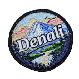 May include: A round, blue and white embroidered patch with a mountain scene and the word "Denali" in white lettering.