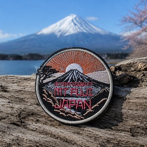 May include: A circular embroidered patch featuring a landscape of Mount Fuji under a sunrise. The design includes a black mountain silhouette, orange sun rays, and white text reading 3776 M 12388 FT, MT FUJI, and JAPAN in red and white thread.