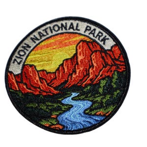 Puede incluir: Parche bordado con un paisaje del Parque Nacional de Zion. El diseño incluye formaciones rocosas rojas, un río azul y el texto "ZION NATIONAL PARK" en un arreglo circular. El parche tiene un borde negro.