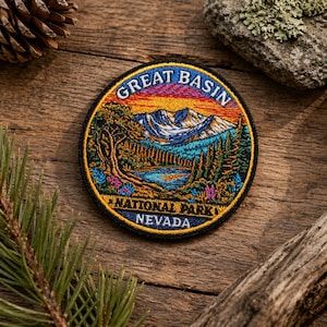 May include: A circular embroidered patch featuring a scenic landscape with mountains, a lake, and trees. The patch reads "GREAT BASIN NATIONAL PARK NEVADA" in a curved font, with a colorful sunset sky background.