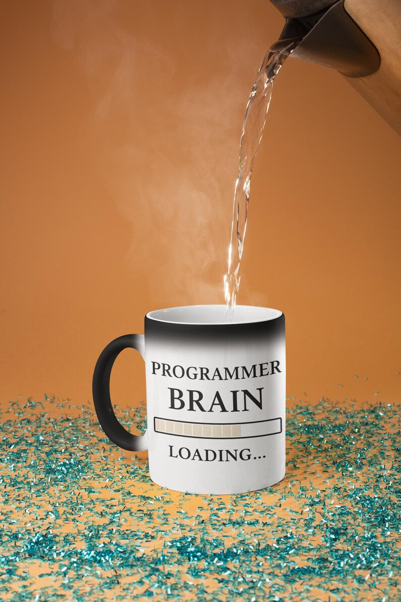 May include: A white coffee mug with the words "PROGRAMMER BRAIN LOADING..." printed on it. Hot water is being poured into the mug. The mug has a black handle and sits on a surface covered in blue confetti.