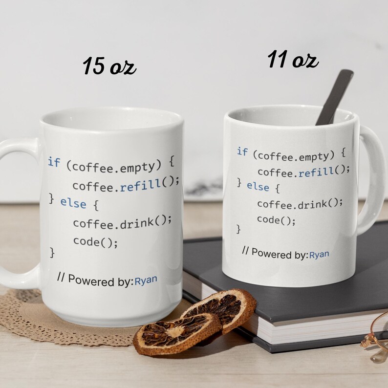 May include: Two white ceramic coffee mugs with black text that reads "if (coffee.empty) { coffee.refill(); } else { coffee.drink(); code(); } // Powered by: Ryan". One mug is labeled 15 oz, the other 11 oz. A spoon rests in one mug.